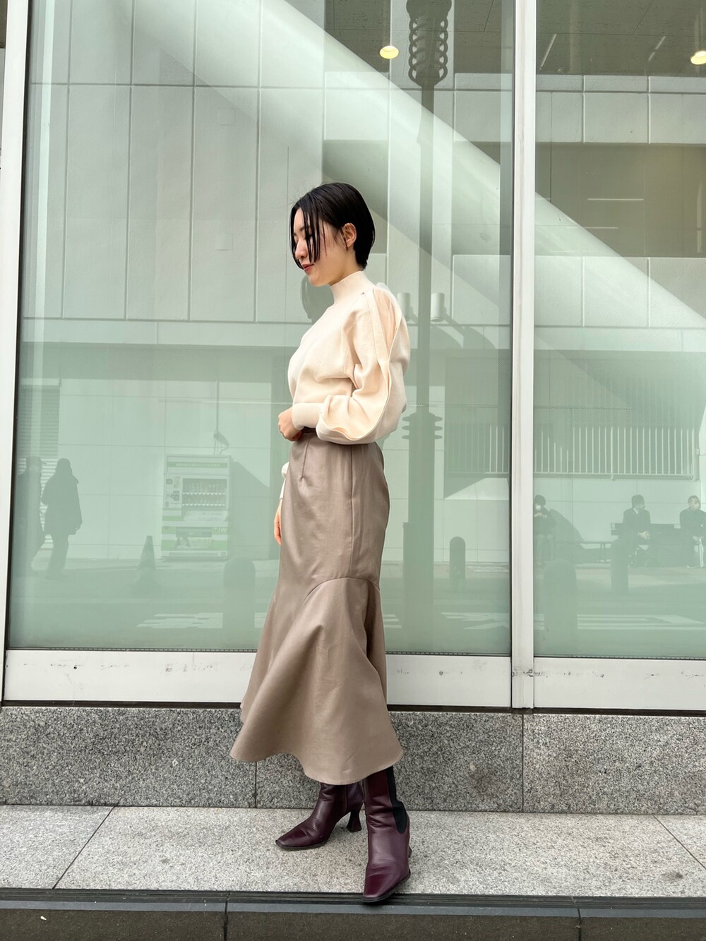 レッド系のブーツ、ベージュ系のスカート、ホワイト系のニット/セーターを着用したレディースの冬コーディネートの2枚目の写真