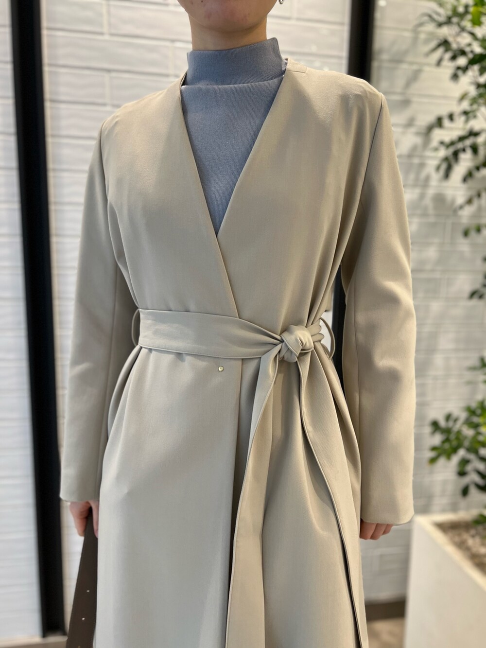 ベージュ系のノーカラーコート、ベージュ系のショルダーバッグ、レッド系のブーツを着用したレディースの冬コーディネートの5枚目の写真