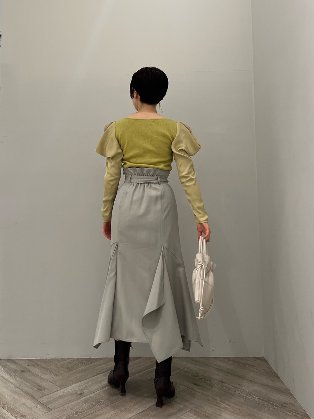 ブラック系のブーツ、ホワイト系のハンドバッグ、グリーン系のスカートを着用したレディースの冬コーディネートの3枚目の写真