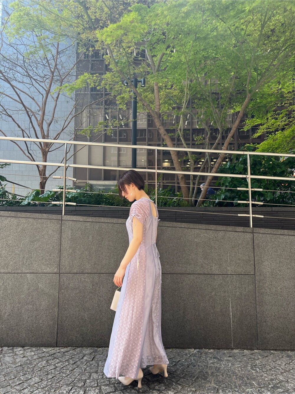 パープル系のドレス、ベージュ系のクラッチバッグ、ベージュ系のパンプスを着用したレディースの春コーディネートの2枚目の写真