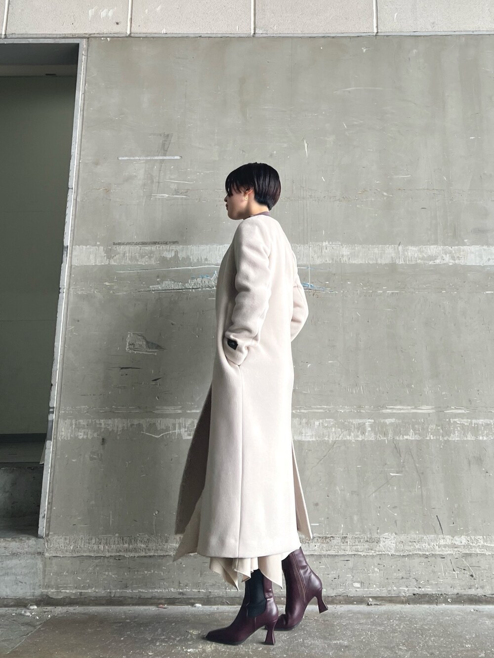 ホワイト系のノーカラーコート、ベージュ系のニット/セーター、ブラウン系のスカートを着用したレディースの秋コーディネートの2枚目の写真