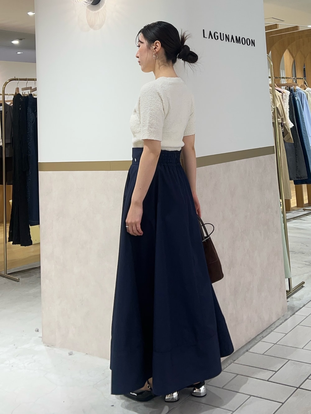 ブルー系のスカート、ホワイト系のニット/セーター、ブラック系のパンプスを着用したレディースの春コーディネートの2枚目の写真