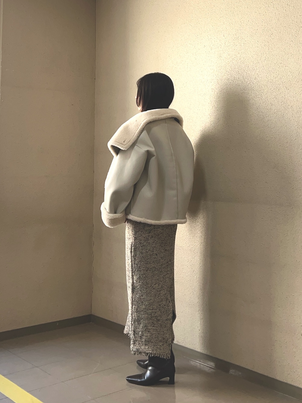 ブラウン系のブーツ、ホワイト系のムートンコート、ベージュ系のジャンパースカートを着用したレディースの秋コーディネートの2枚目の写真