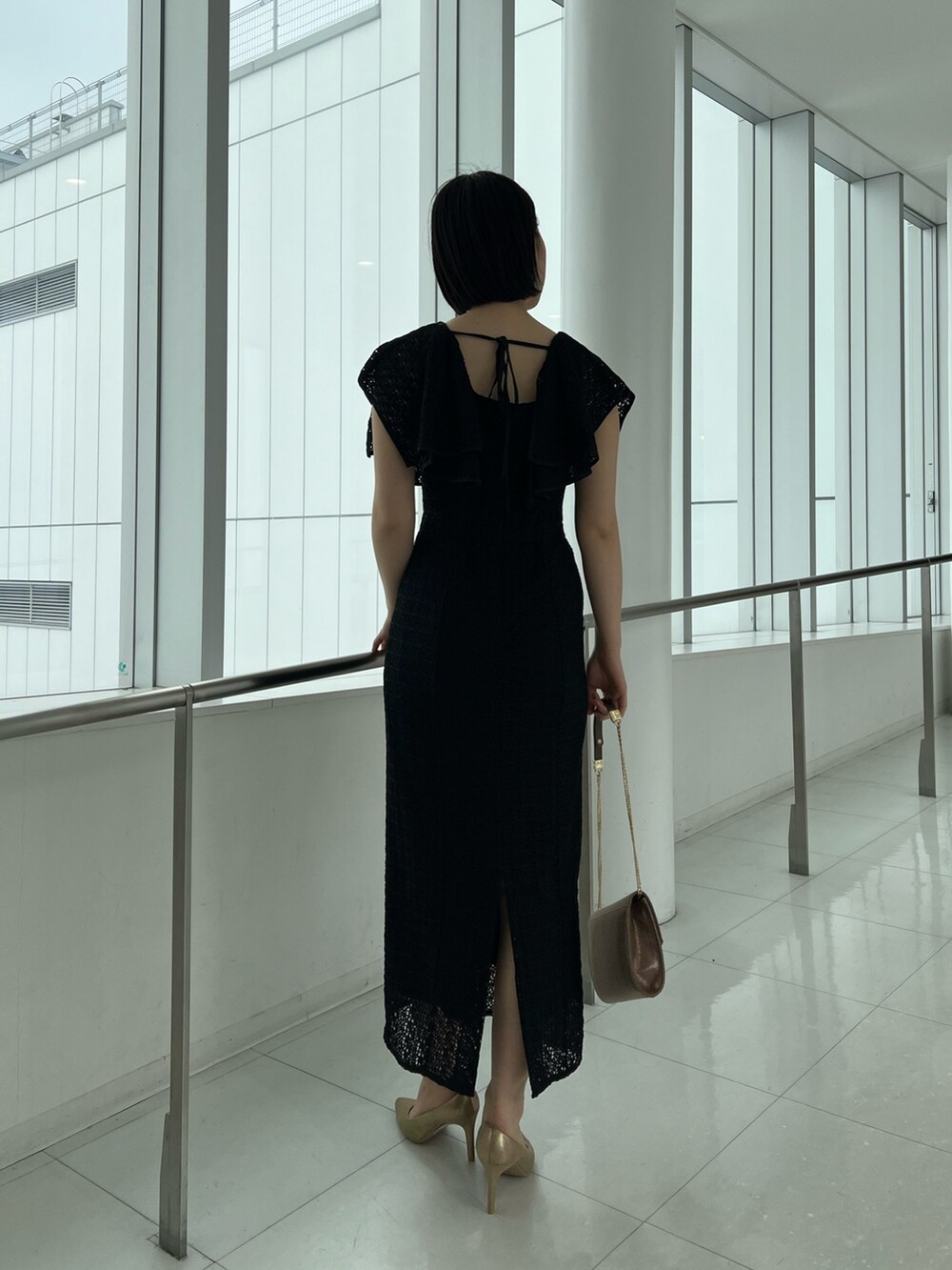 ゴールド系のハンドバッグ、ゴールド系のパンプス、ブラック系のワンピースを着用したレディースの春コーディネートの2枚目の写真