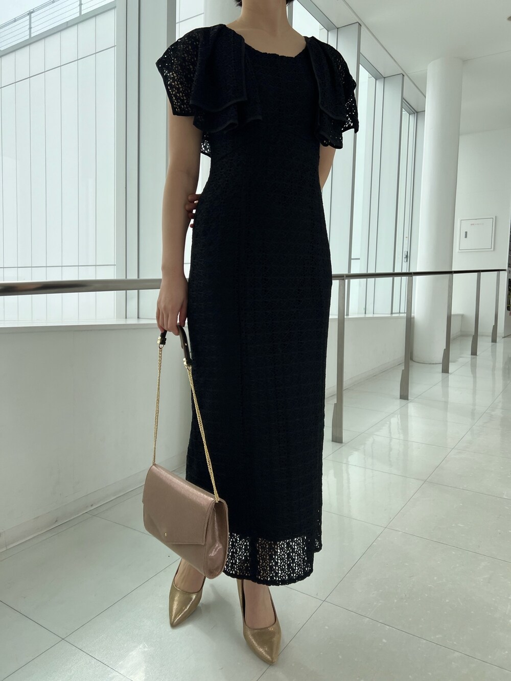 ゴールド系のハンドバッグ、ゴールド系のパンプス、ブラック系のワンピースを着用したレディースの春コーディネートの5枚目の写真