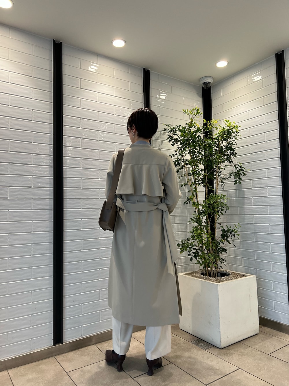 ベージュ系のノーカラーコート、ベージュ系のショルダーバッグ、レッド系のブーツを着用したレディースの冬コーディネートの3枚目の写真