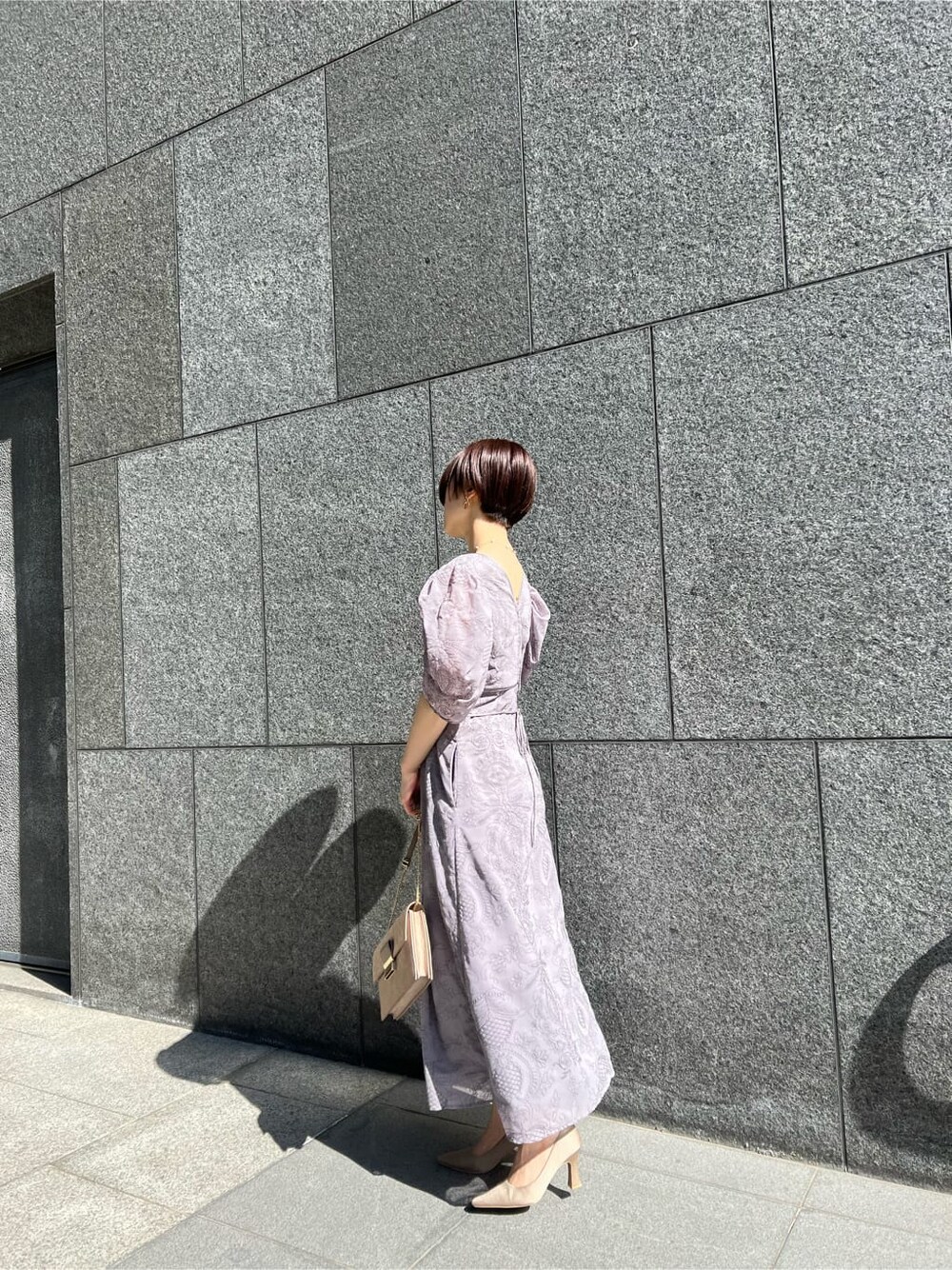 ブラウン系のクラッチバッグ、ベージュ系のその他アウター、パープル系のドレスを着用したレディースの冬コーディネートの4枚目の写真