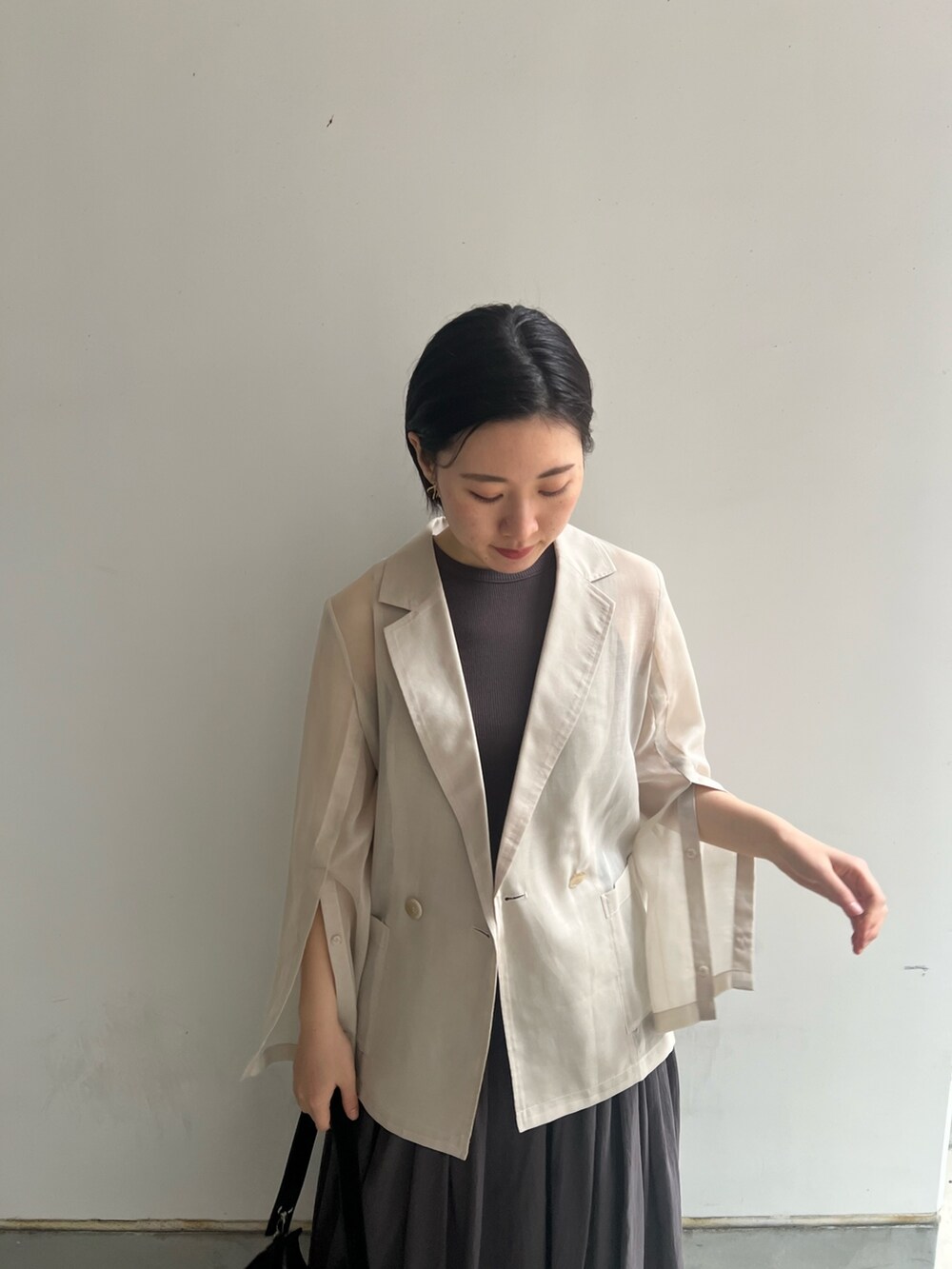 ブラック系のハンドバッグ、グレー系のワンピース、ホワイト系のテーラードジャケットを着用したレディースの春コーディネートの2枚目の写真