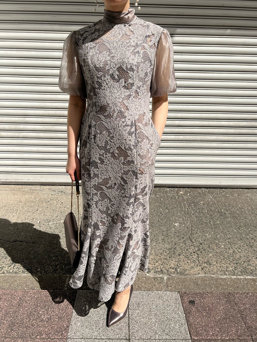 ブルー系のノーカラーコート、シルバー系のパンプス、シルバー系のクラッチバッグを着用したレディースの春コーディネートの7枚目の写真