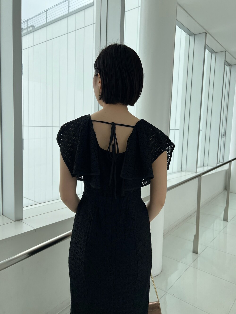 ゴールド系のハンドバッグ、ゴールド系のパンプス、ブラック系のワンピースを着用したレディースの春コーディネートの4枚目の写真