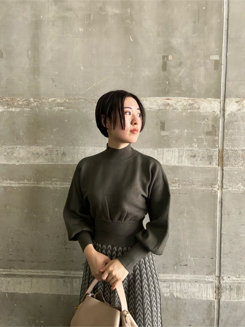 ベージュ系のブーツ、ベージュ系のハンドバッグ、ベージュ系のワンピースを着用したレディースの秋コーディネートの4枚目の写真