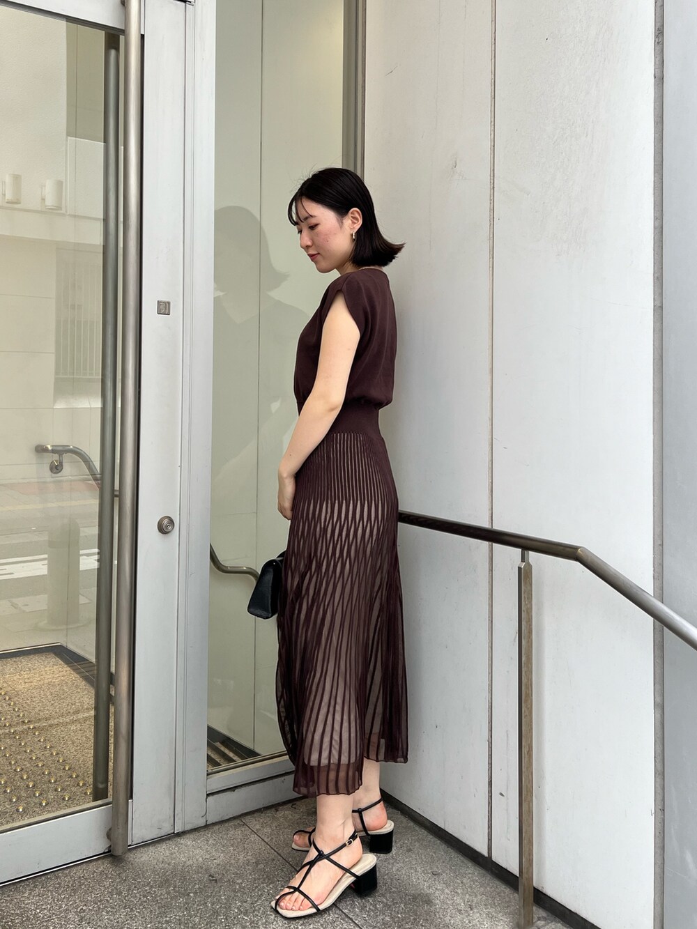 ブラック系のサンダル、ブラック系のハンドバッグ、ブラウン系のワンピースを着用したレディースの夏コーディネートの2枚目の写真