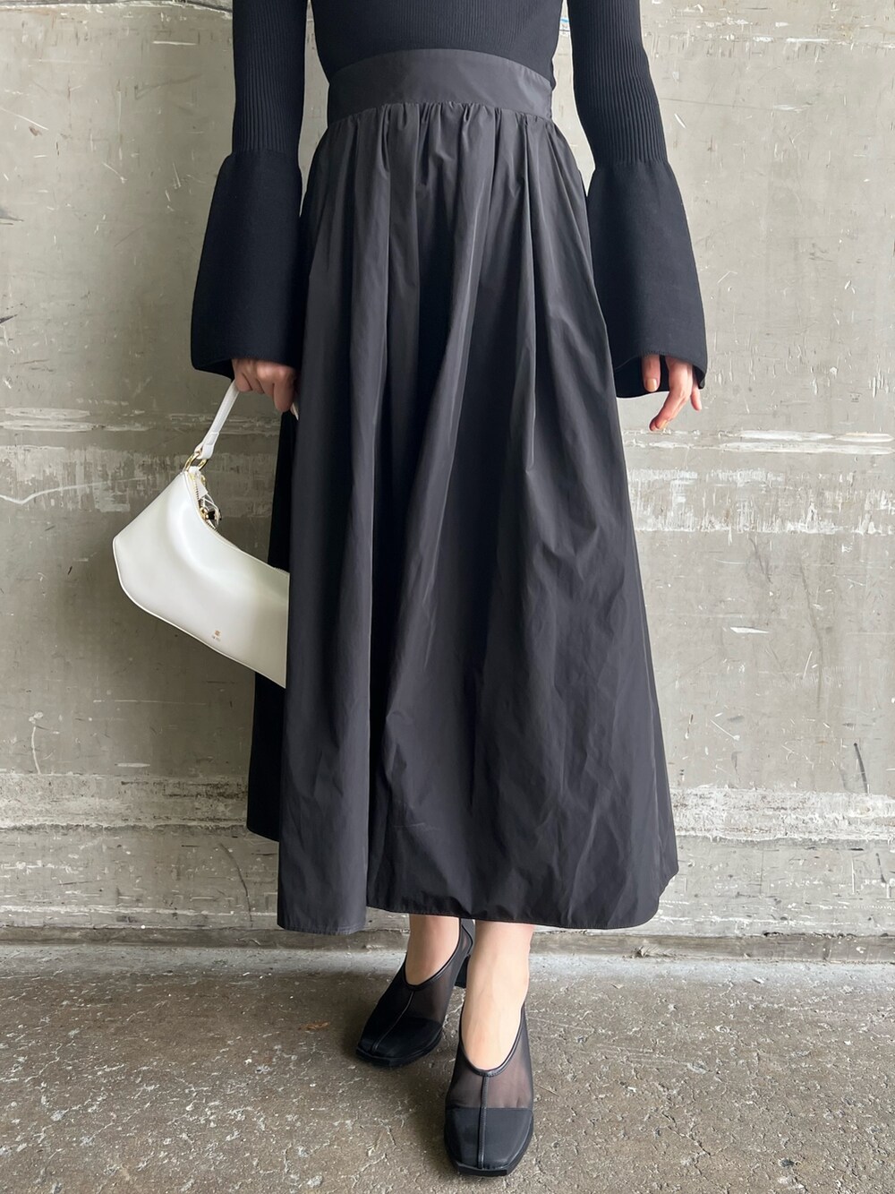 ホワイト系のハンドバッグ、ブラック系のワンピース、ブラック系のパンプスを着用したレディースの秋コーディネートの7枚目の写真