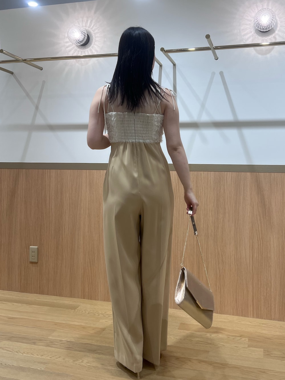 ベージュ系のパンツドレス、ゴールド系のパンプス、ゴールド系のクラッチバッグを着用したレディースの春コーディネートの3枚目の写真