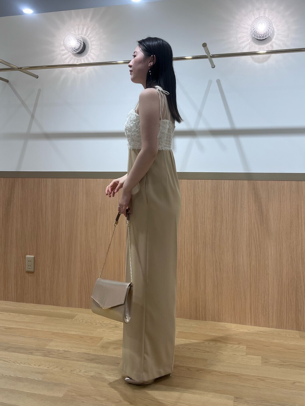 ベージュ系のパンツドレス、ゴールド系のパンプス、ゴールド系のクラッチバッグを着用したレディースの春コーディネートの2枚目の写真