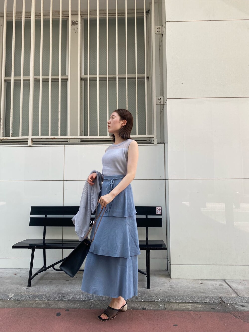 ブラック系のハンドバッグ、ブルー系のスカート、グレー系のニット/セーターを着用したレディースの夏コーディネートの3枚目の写真