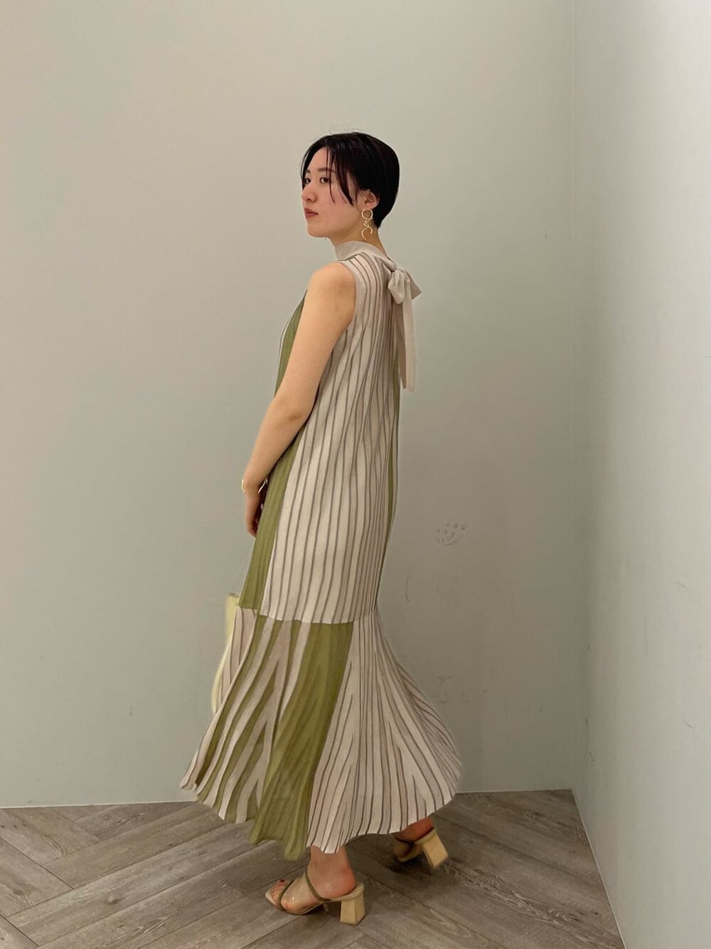 グリーン系のワンピース、グリーン系のサンダル、ゴールド系のピアス（両耳用）を着用したレディースの夏コーディネートの2枚目の写真