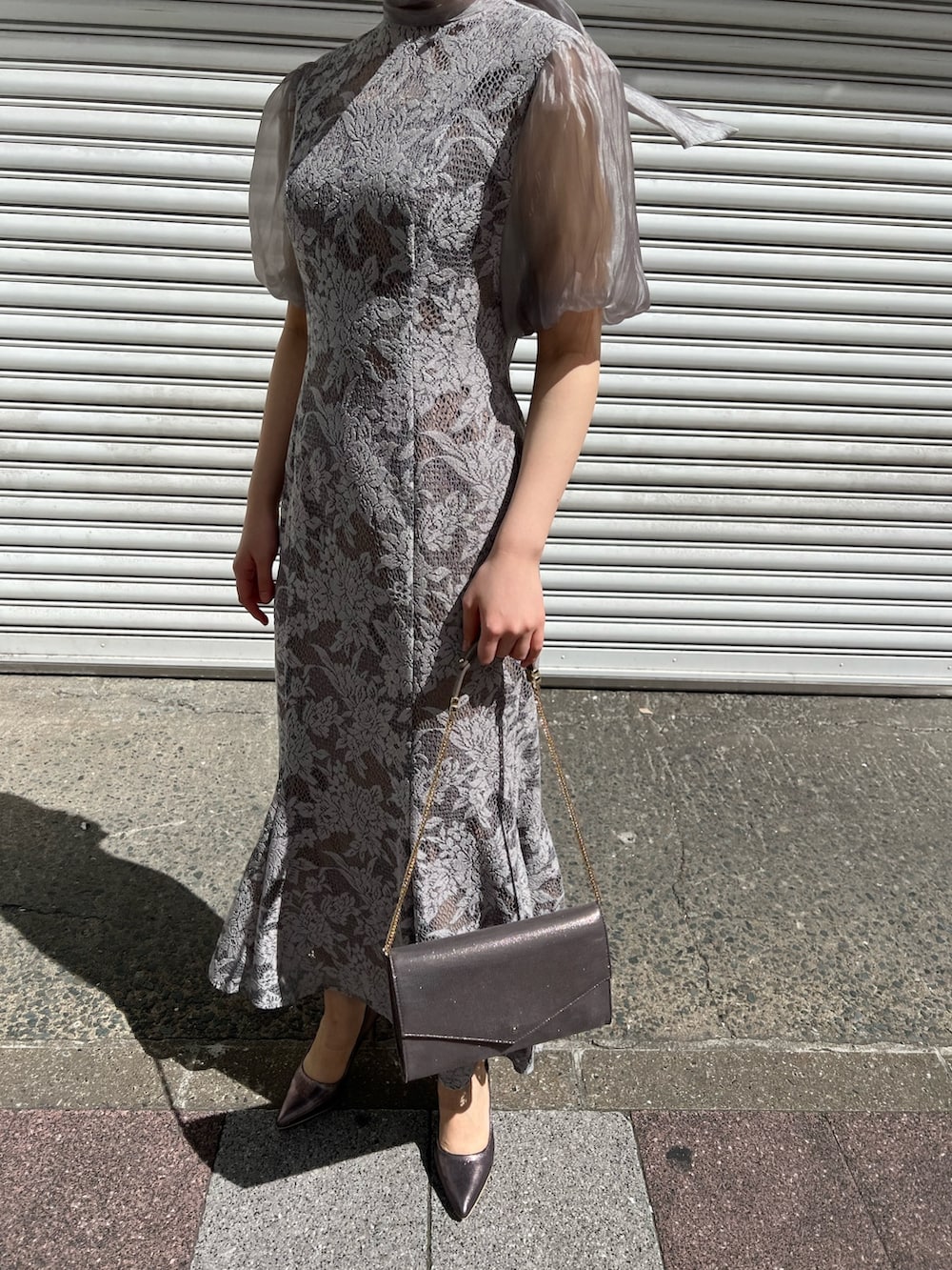 ブルー系のノーカラーコート、シルバー系のパンプス、シルバー系のクラッチバッグを着用したレディースの春コーディネートの6枚目の写真