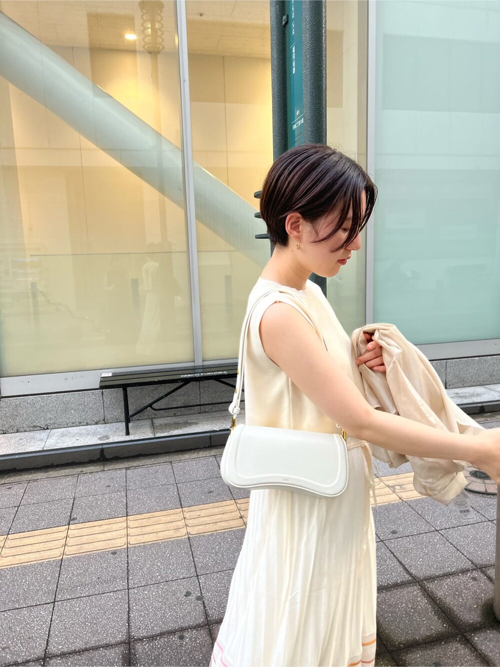 ホワイト系のワンピース、ホワイト系のショルダーバッグ、ゴールド系のピアス（両耳用）を着用したレディースの夏コーディネートの4枚目の写真