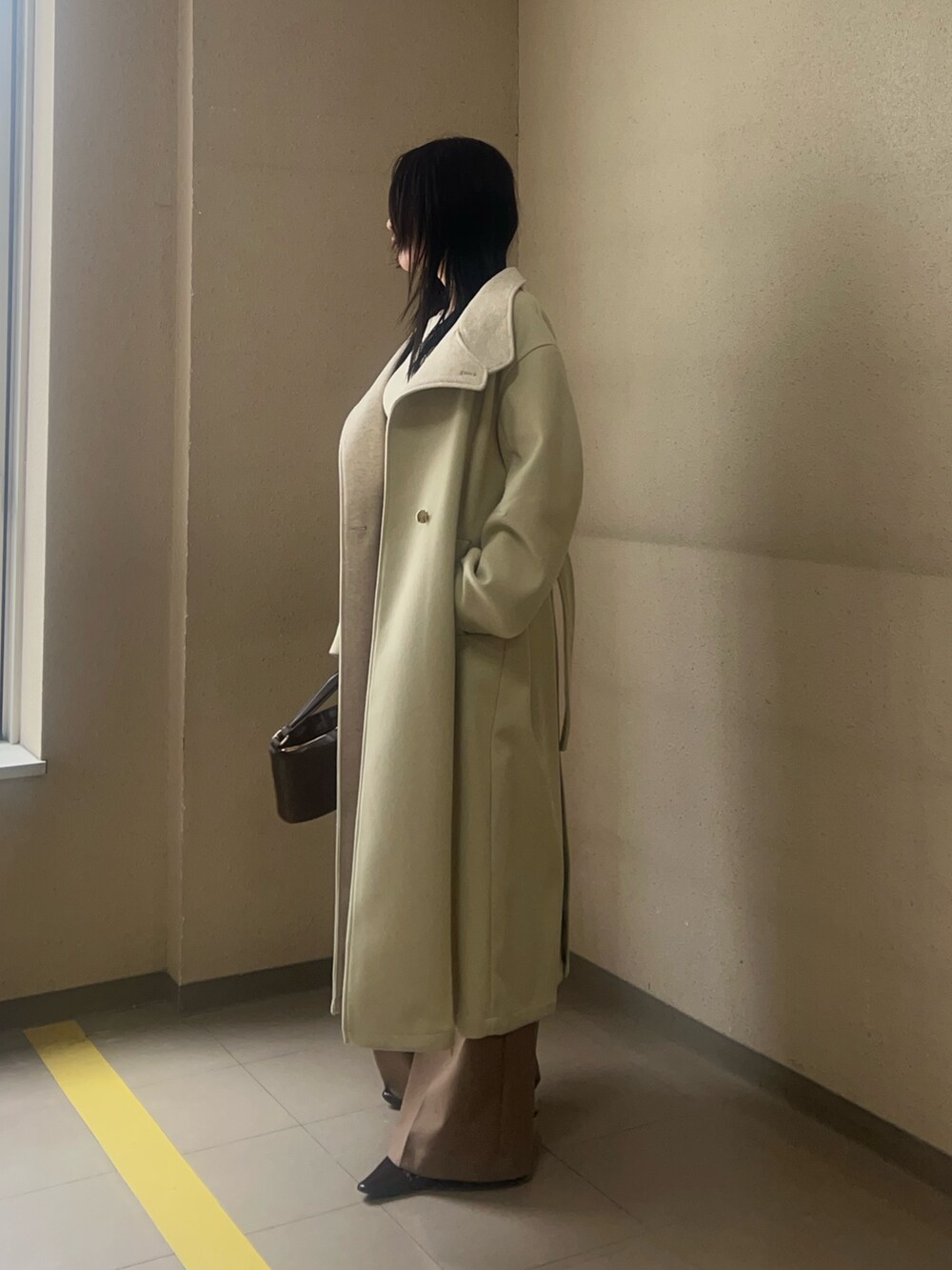 グリーン系のチェスターコート、ブラウン系のハンドバッグ、ブラウン系のその他パンツを着用したレディースの秋コーディネートの2枚目の写真