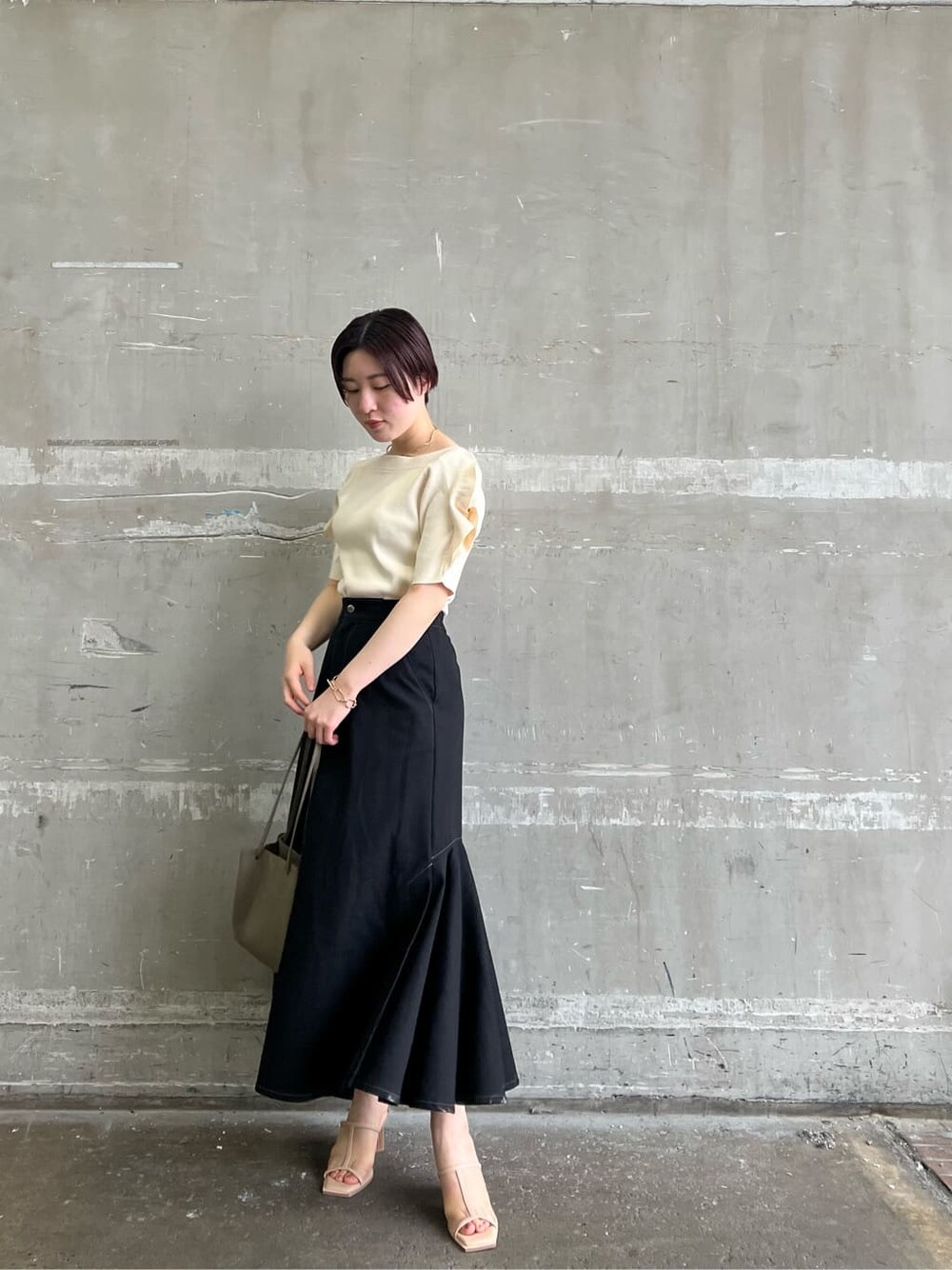 ベージュ系のハンドバッグ、ブラック系のスカート、ホワイト系のニット/セーターを着用したレディースの夏コーディネートの2枚目の写真