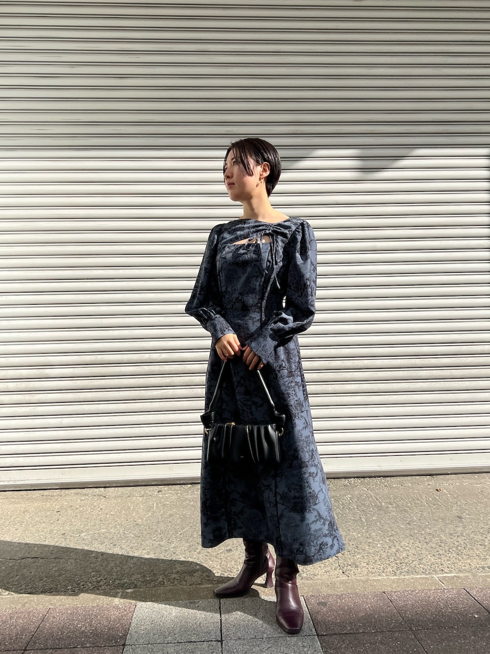 レッド系のブーツ、ブラック系のノーカラーコート、ブルー系のワンピースを着用したレディースの冬コーディネートの3枚目の写真