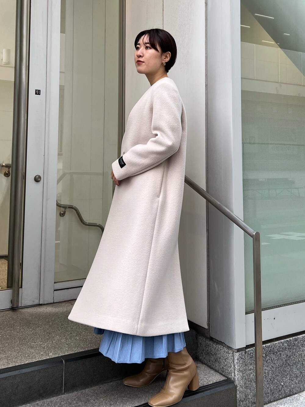 ベージュ系のブーツ、ホワイト系のハンドバッグ、ホワイト系のノーカラーコートを着用したレディースの冬コーディネートの2枚目の写真