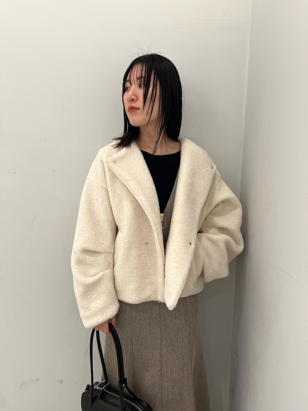 ホワイト系のブルゾン、ベージュ系のジャンパースカート、ブラック系のニット/セーターを着用したレディースの冬コーディネートの4枚目の写真