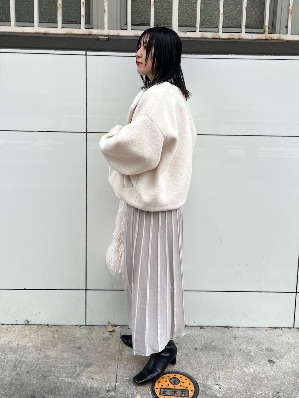 ホワイト系のブルゾン、グレー系のワンピース、ホワイト系のハンドバッグを着用したレディースの冬コーディネートの2枚目の写真