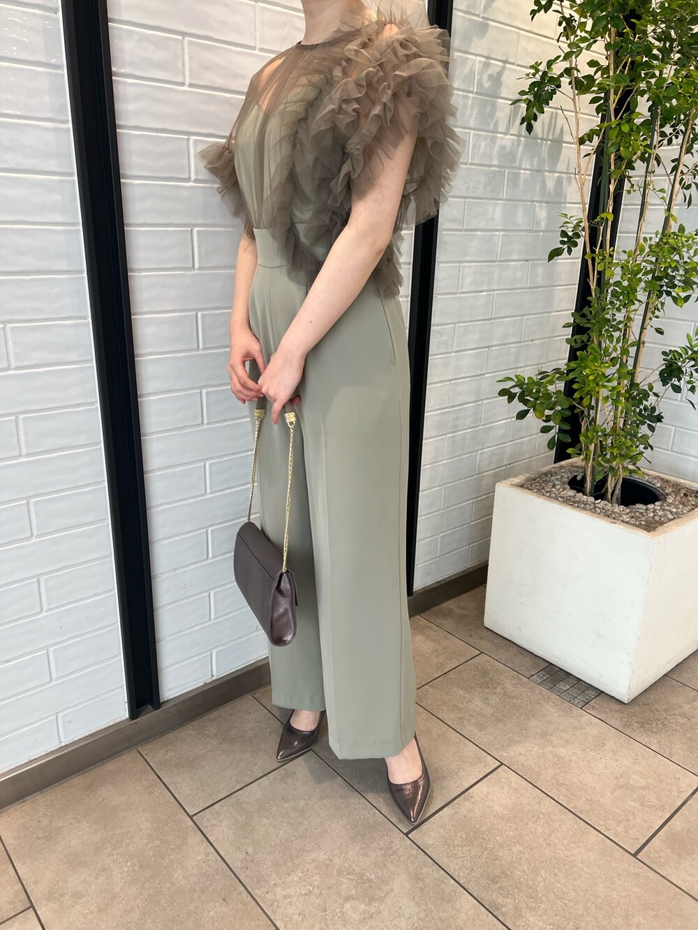 シルバー系のパンプス、シルバー系のハンドバッグ、グリーン系のパンツドレスを着用したレディースの春コーディネートの6枚目の写真