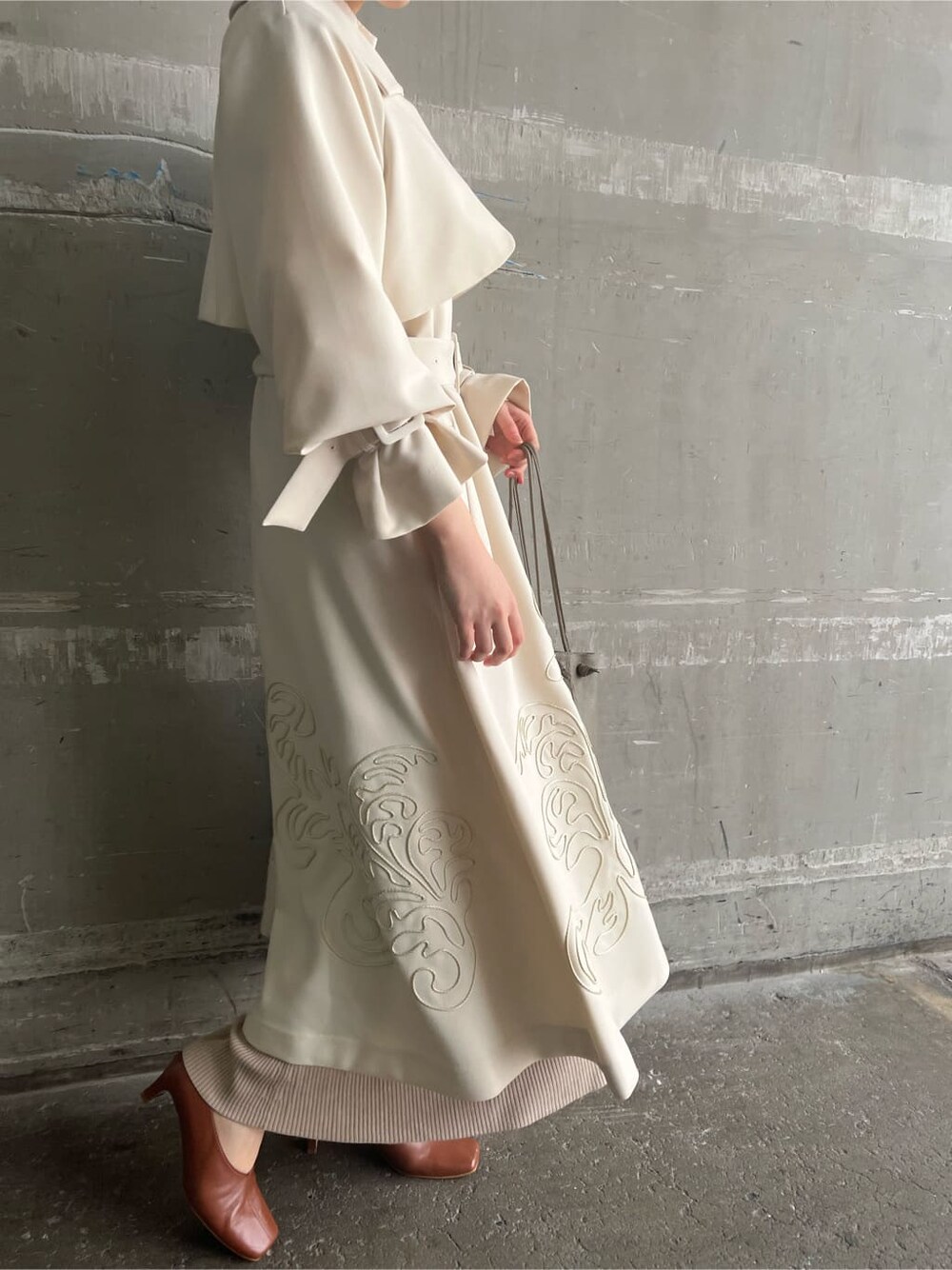 ホワイト系のトレンチコート、ベージュ系のワンピース、ベージュ系のハンドバッグを着用したレディースの春コーディネートの3枚目の写真