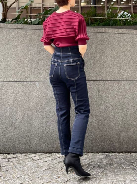 ブラック系のブーツ、レッド系のニット/セーター、ブルー系のデニムパンツを着用したレディースの秋コーディネートの2枚目の写真