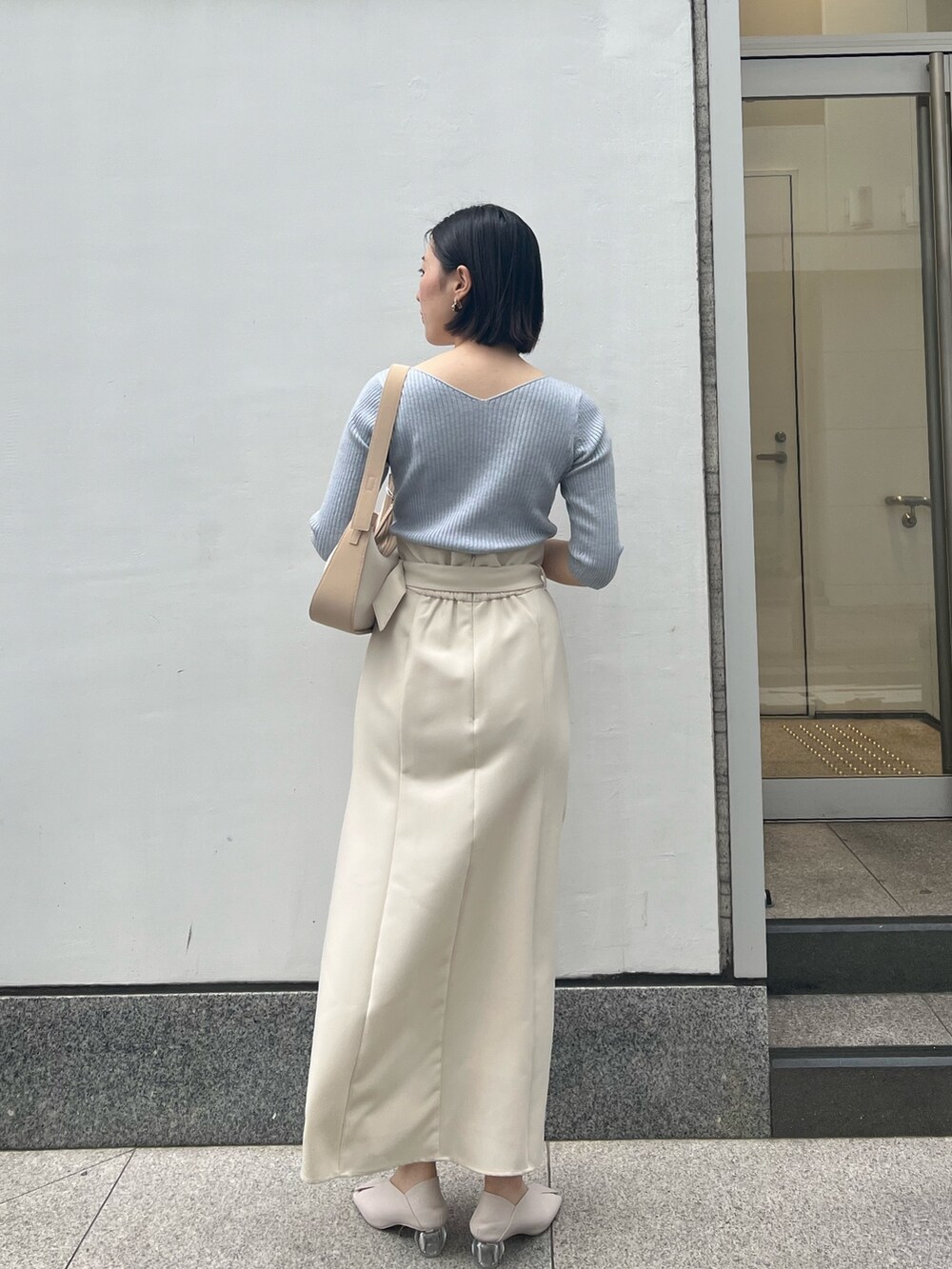 ホワイト系のパンプス、ベージュ系のハンドバッグ、ブルー系のニット/セーターを着用したレディースの春コーディネートの2枚目の写真