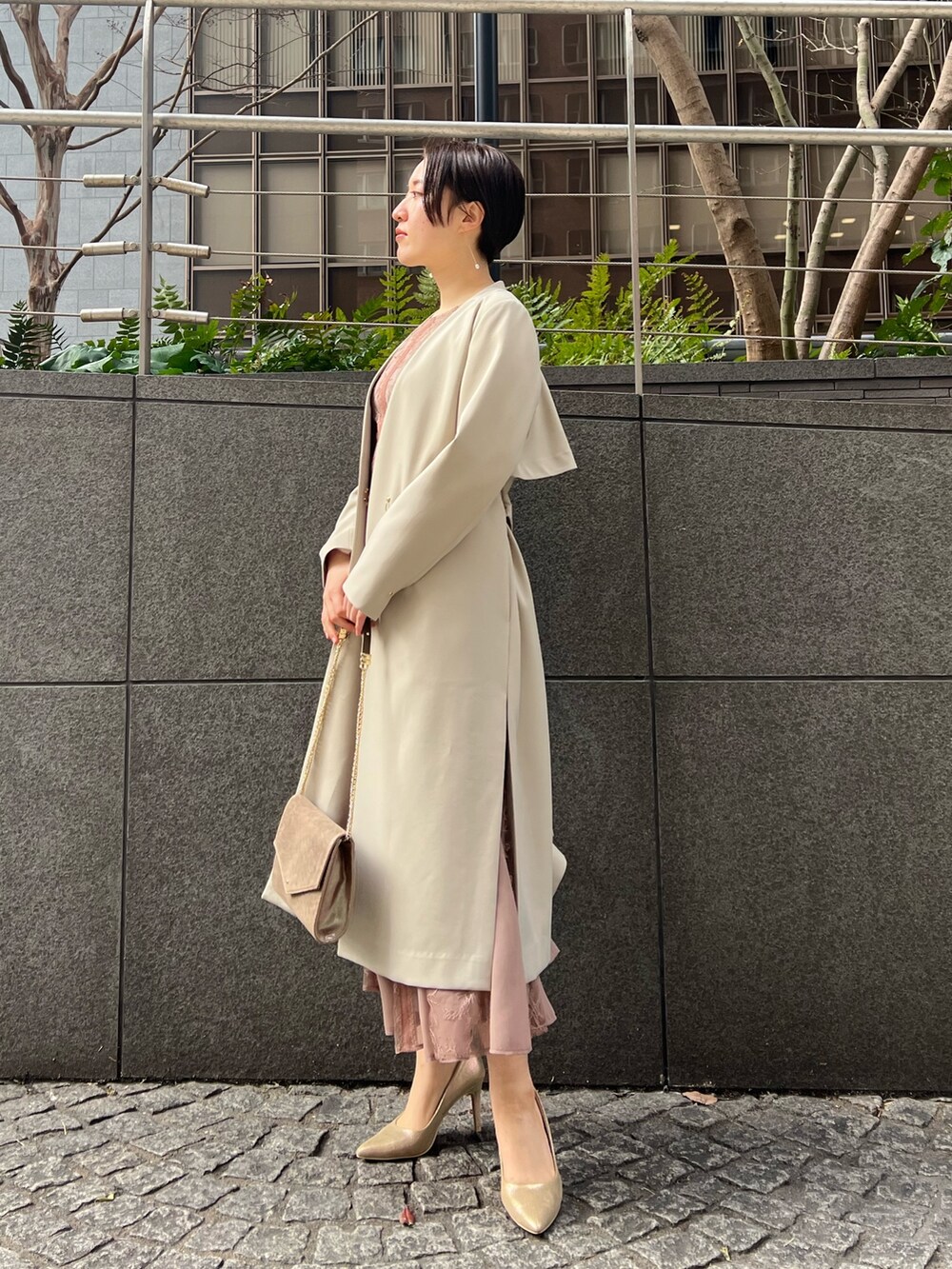 ゴールド系のハンドバッグ、ゴールド系のパンプス、ベージュ系のノーカラーコートを着用したレディースの冬コーディネートの3枚目の写真