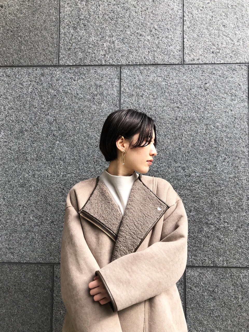 ベージュ系のムートンコート、グレー系のニット/セーター、ゴールド系のピアス（両耳用）を着用したレディースの冬コーディネートの2枚目の写真