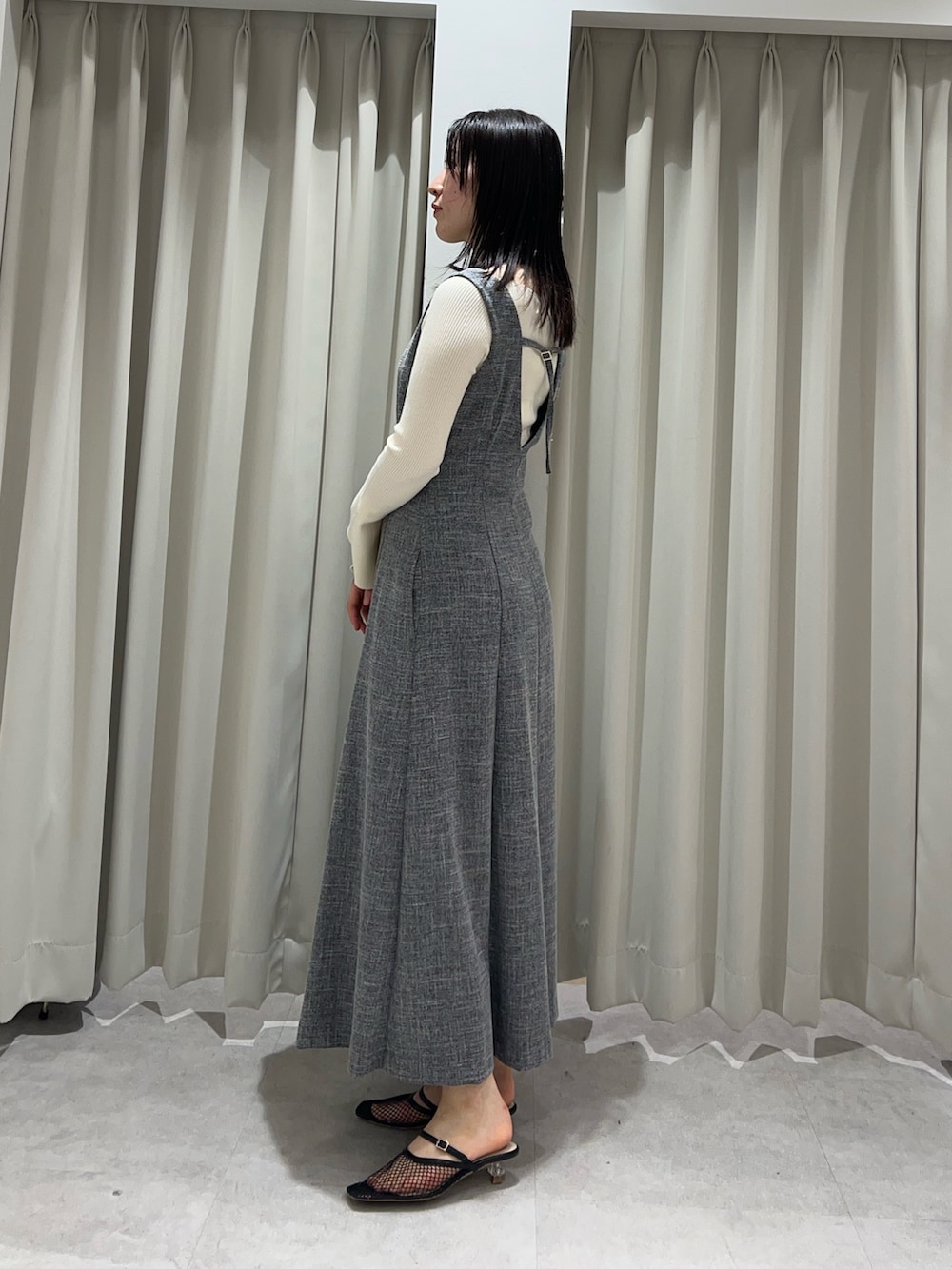 ホワイト系のニット/セーター、グレー系のジャンパースカート、ブラック系のサンダルを着用したレディースの春コーディネートの2枚目の写真