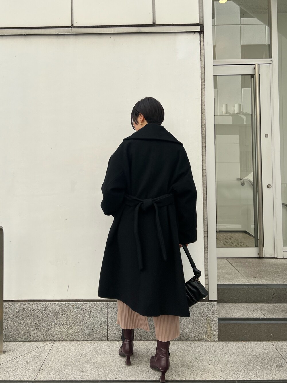 レッド系のブーツ、ブラック系のハンドバッグ、ベージュ系のワンピースを着用したレディースの冬コーディネートの2枚目の写真