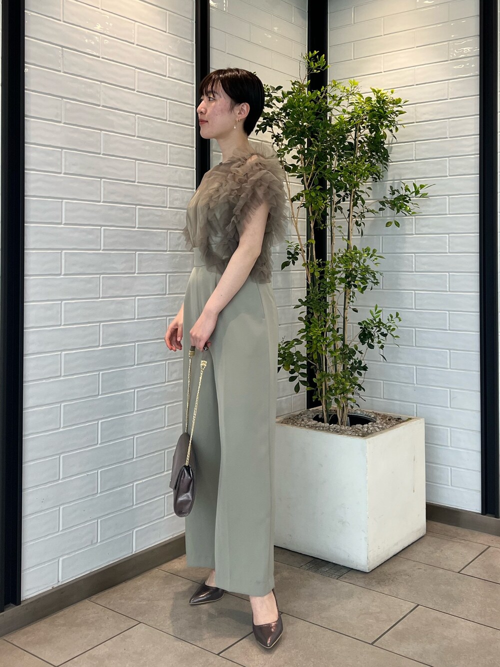 シルバー系のパンプス、シルバー系のハンドバッグ、グリーン系のパンツドレスを着用したレディースの春コーディネートの2枚目の写真