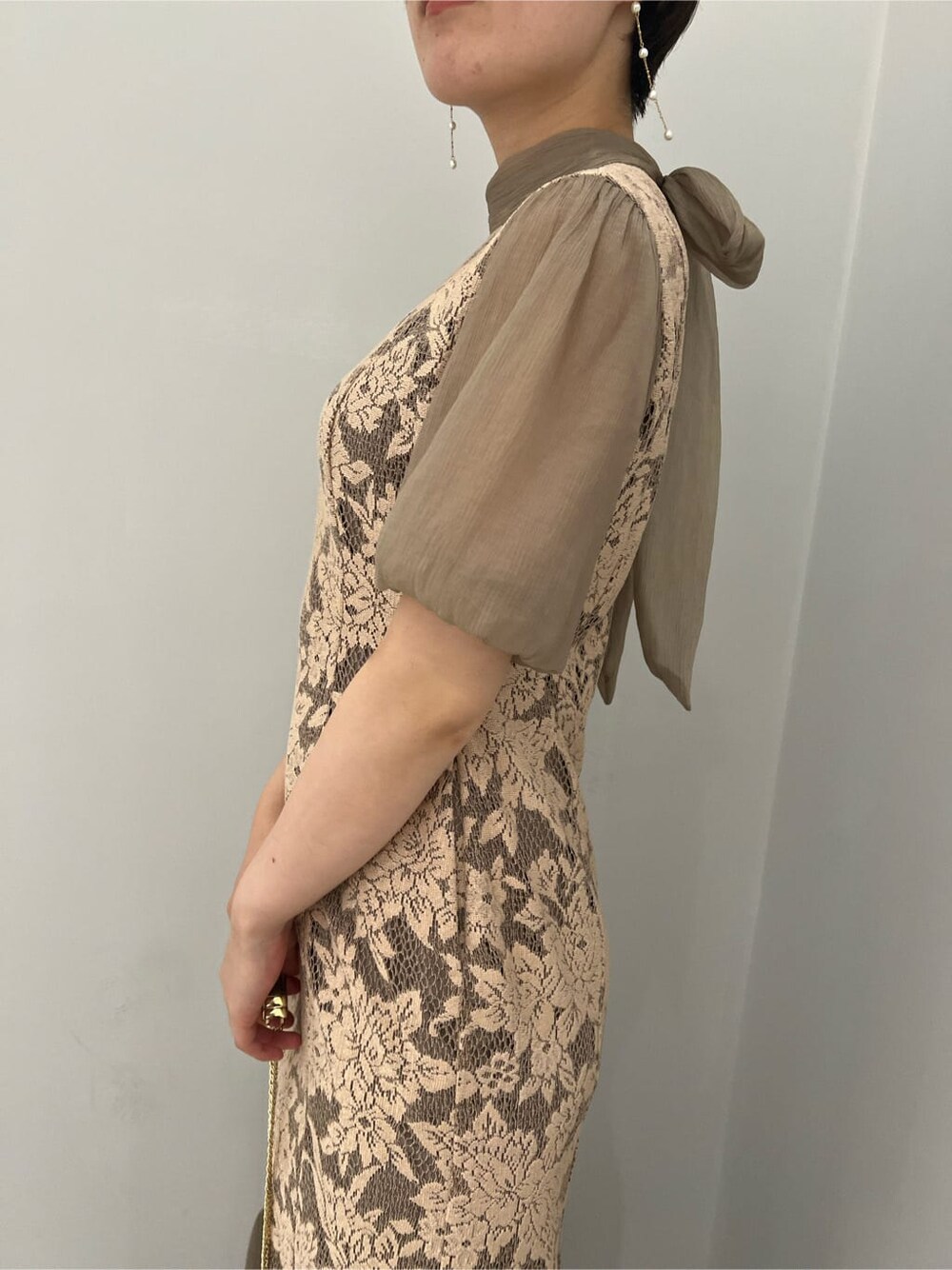 ゴールド系のクラッチバッグ、ゴールド系のパンプス、ベージュ系のドレスを着用したレディースの夏コーディネートの5枚目の写真