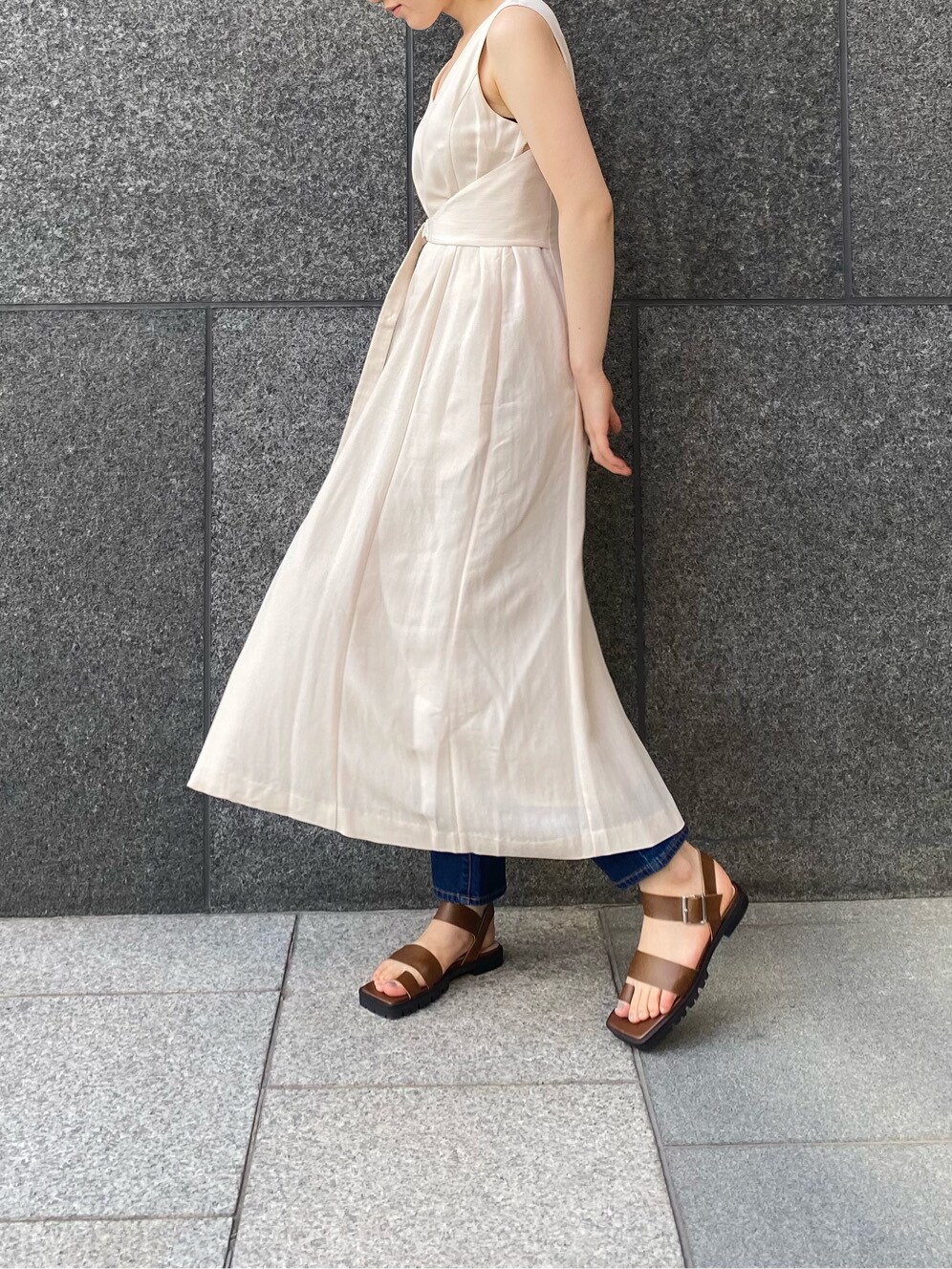 ブルー系のデニムパンツ、ブラウン系のサンダル、ベージュ系のワンピースを着用したレディースの春コーディネートの2枚目の写真