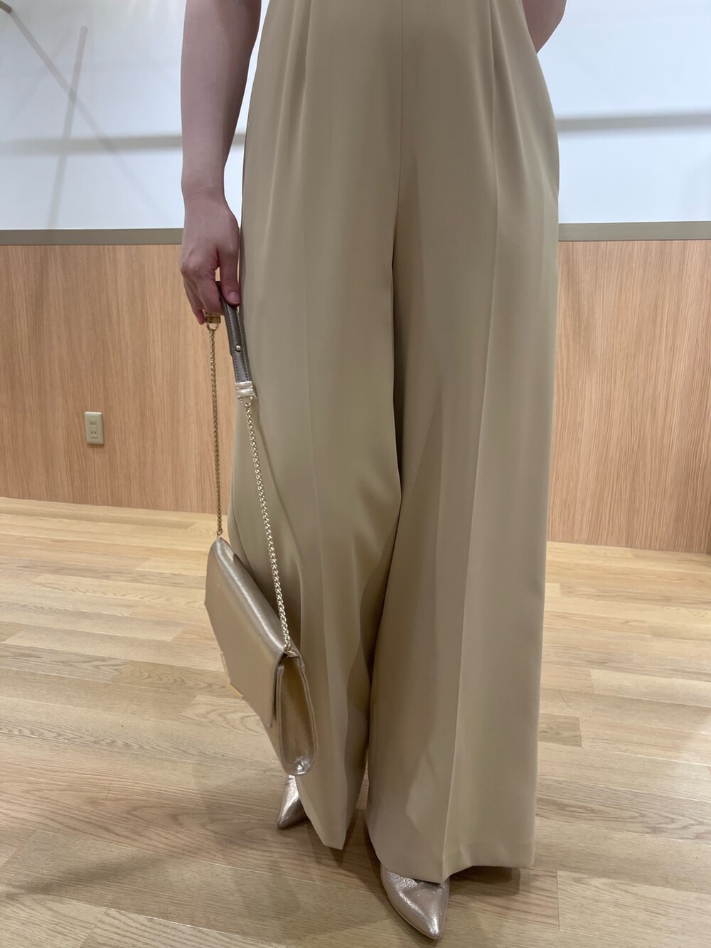 ベージュ系のパンツドレス、ゴールド系のパンプス、ゴールド系のクラッチバッグを着用したレディースの春コーディネートの6枚目の写真