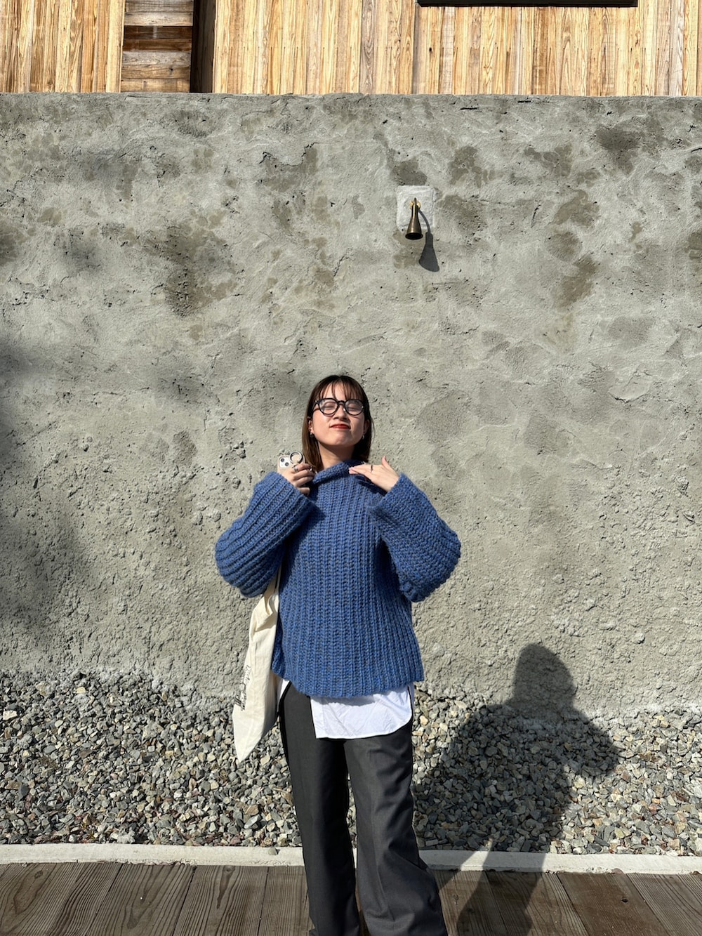 ホワイト系のトートバッグ、ブルー系のニット/セーター、グレー系のスラックスを着用したレディースの春コーディネートの2枚目の写真