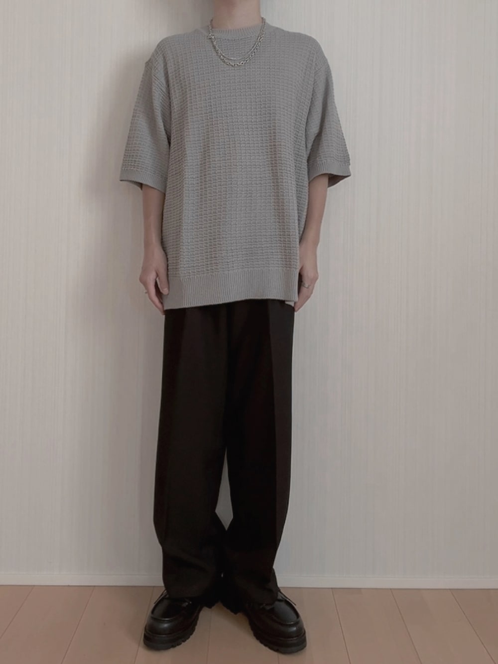 グレー系のニット/セーター、ブラック系のスラックス、ブラック系のモカシン/デッキシューズを着用したメンズの夏コーディネートの3枚目の写真