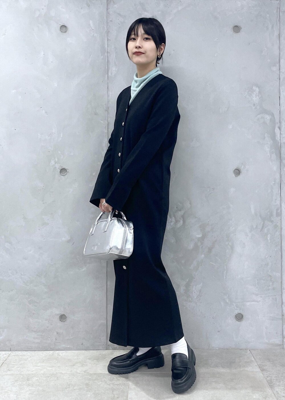 ブラック系のローファー、グリーン系のニット/セーター、シルバー系のショルダーバッグを着用したレディースの冬コーディネートの3枚目の写真