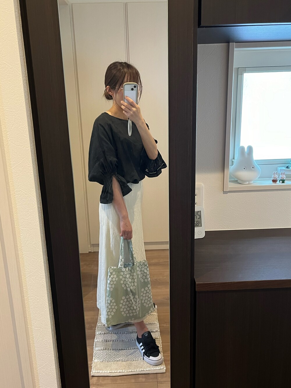 グリーン系のトートバッグ、ホワイト系のスカート、ブラック系のトップスを着用したレディースの春コーディネートの2枚目の写真