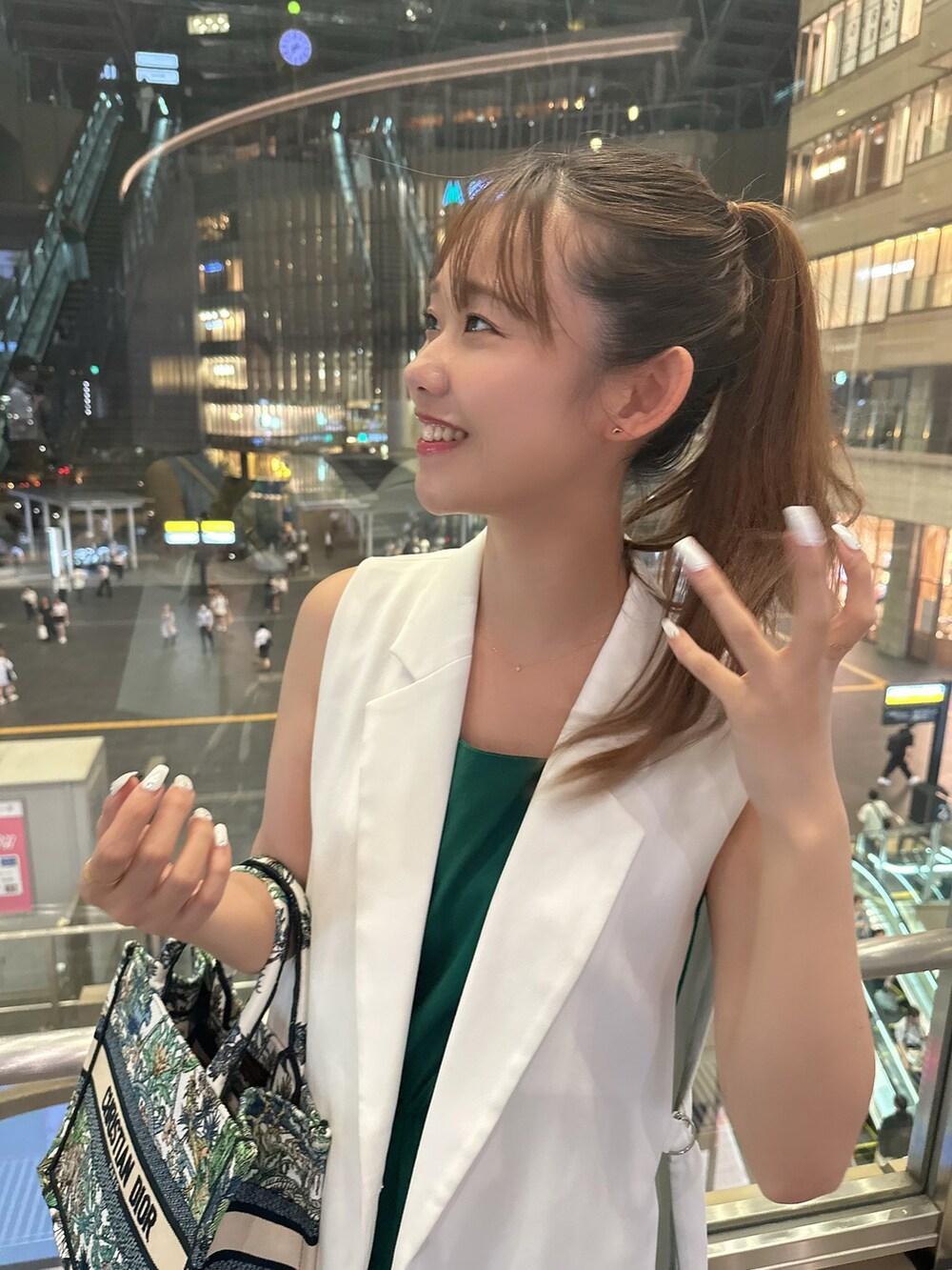 グリーン系のトートバッグ、ブラック系のパンプス、ホワイト系のベストを着用したレディースの夏コーディネートの2枚目の写真