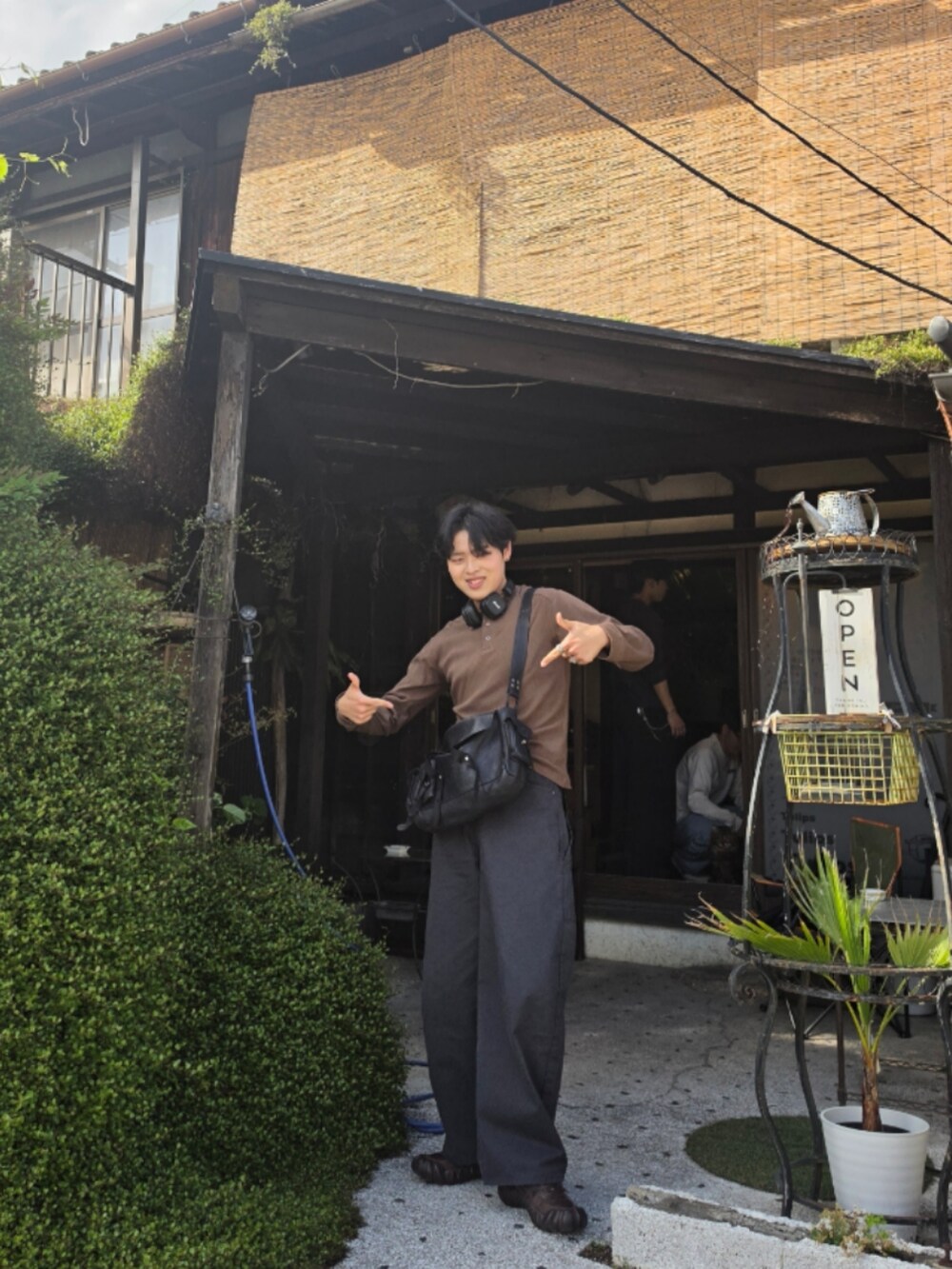 グレー系のパンツ、ブラウン系のトップス、ブラック系のショルダーバッグを着用したメンズの春コーディネートの2枚目の写真