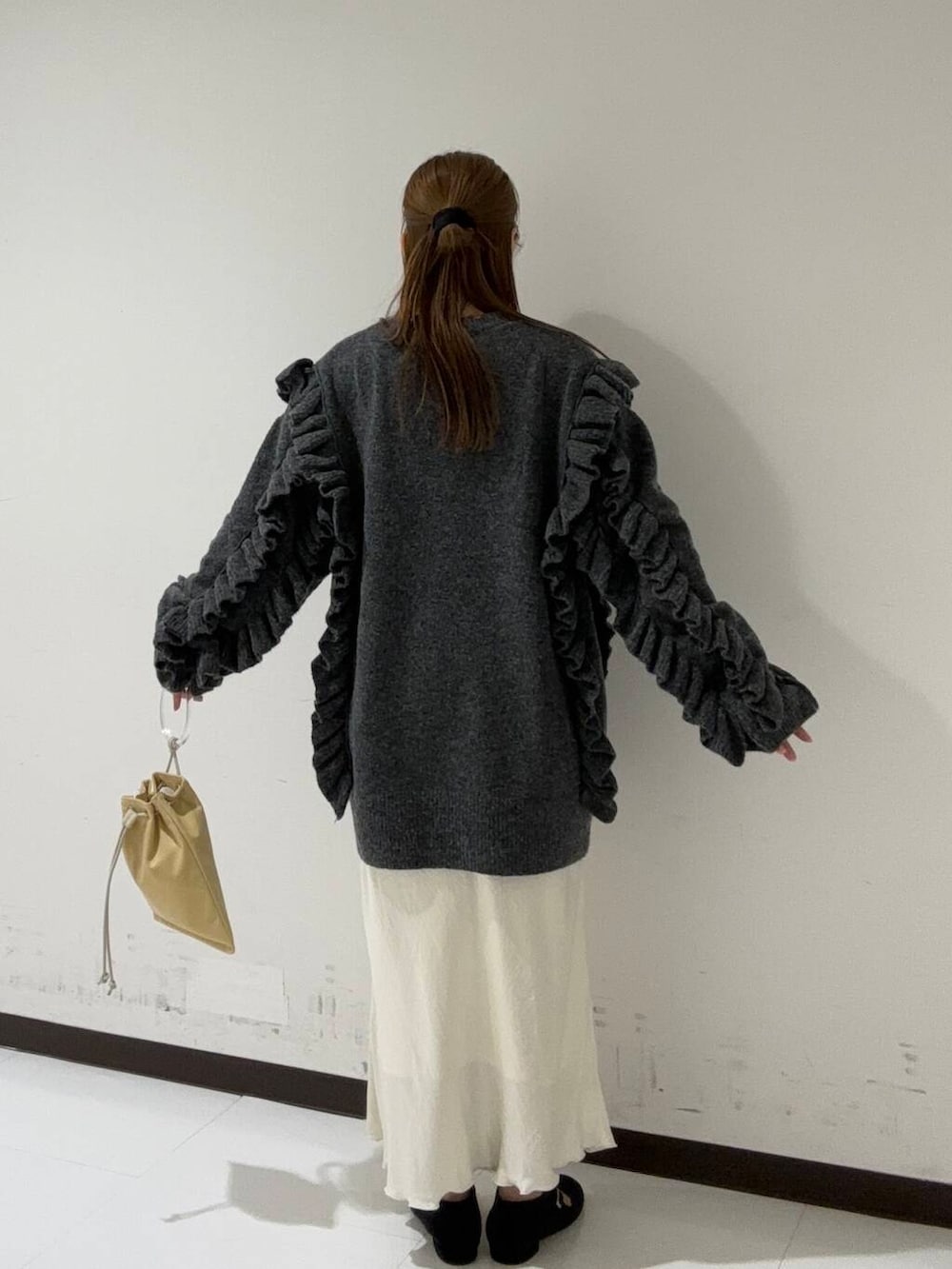 イエロー系のショルダーバッグ、ホワイト系のスカート、グレー系のニット/セーターを着用したレディースの冬コーディネートの3枚目の写真