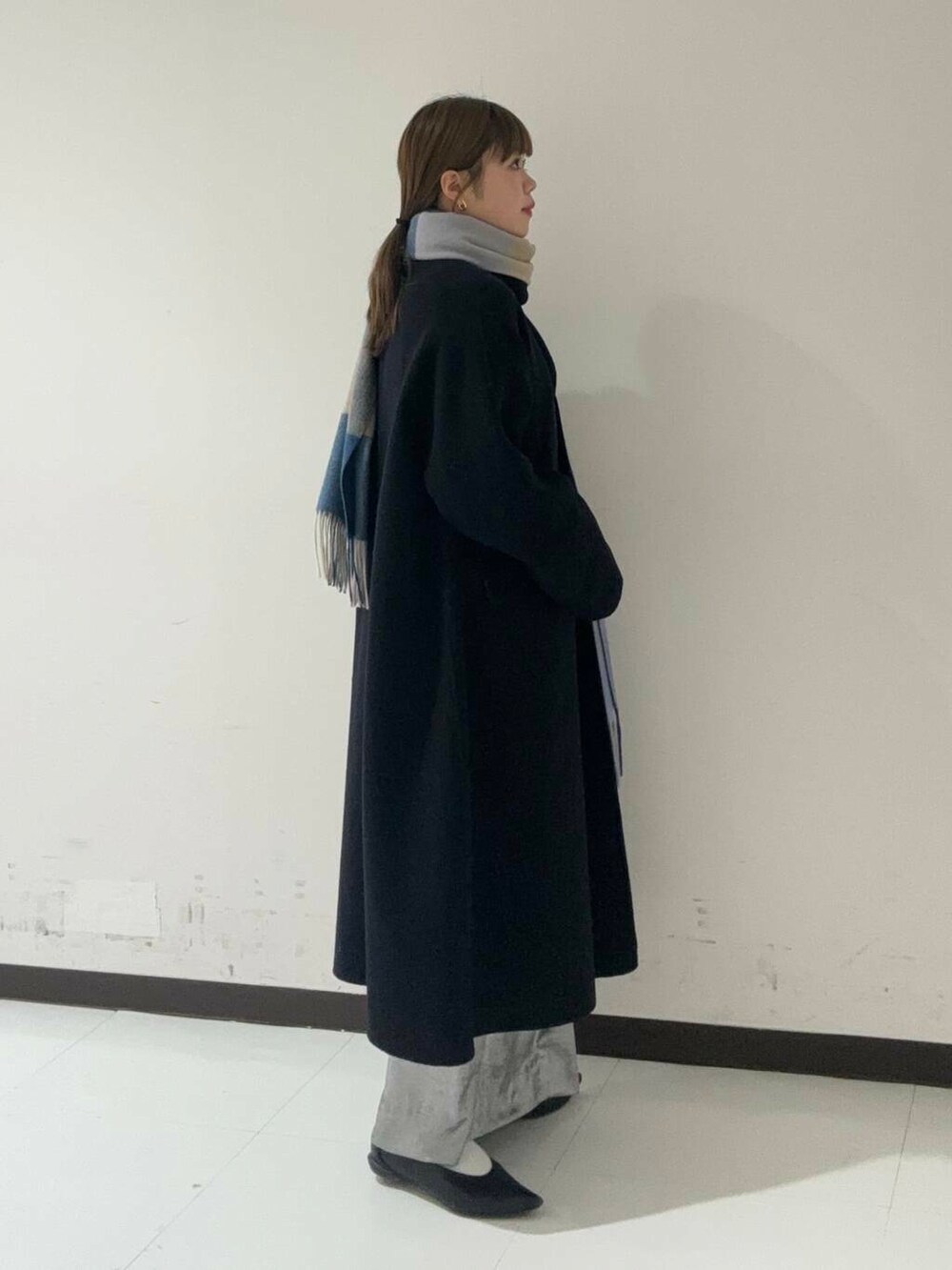 ブラック系のステンカラーコート、シルバー系のスカート、グレー系のニット/セーターを着用したレディースの冬コーディネートの2枚目の写真