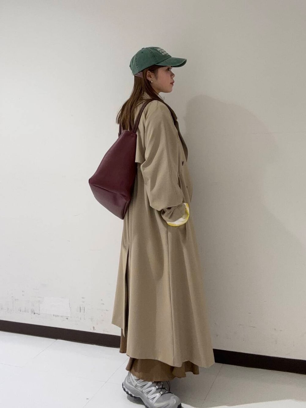 イエロー系のスカート、ベージュ系のトレンチコート、イエロー系のTシャツ/カットソーを着用したレディースの冬コーディネートの2枚目の写真